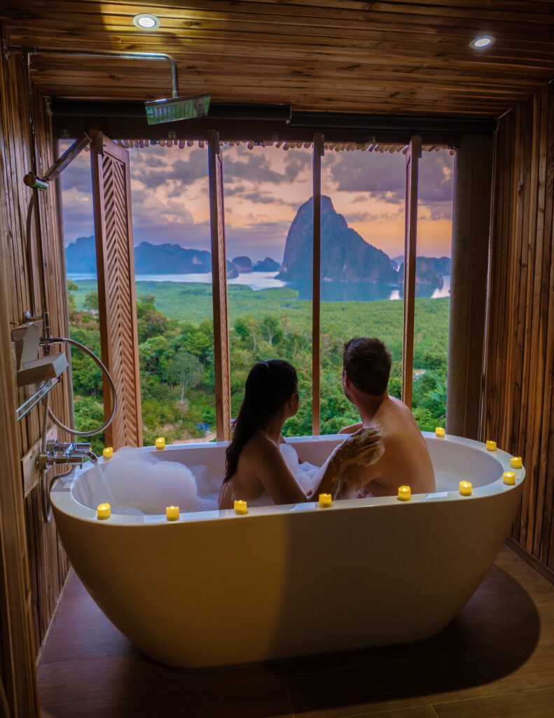 Couple in tub with beautiful view of Thailand landscape through open window. A spontaneous travel idea.